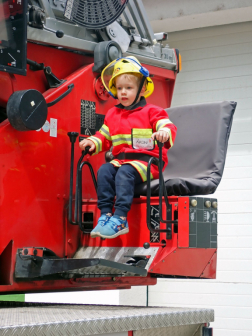 Tűzoltóruhába öltözött kisfiú a magasból mentő kezelőállásában