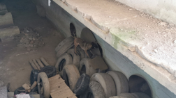 Egy belga juhász teherautóabroncsokon állva ugat befelé egy kerek, vaslemezzel lefedett nyílás felé