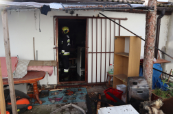 egy tűzoltó áll a kiégett szoba bejáratában, az épület előtt a házból kimentett szőnyegek, bútorok láthatók