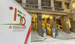 A Belügyminisztérium aulája, előtérben a 150 éves jubilium logója, háttérben a márványterembe vezető átjáró két oldalán posztoló, régi tűzoltóruhát viselő kollégák